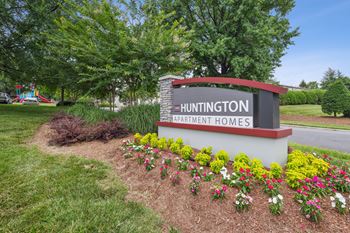 A sign for Huntington Apartment Homes is surrounded by flowers and greenery.